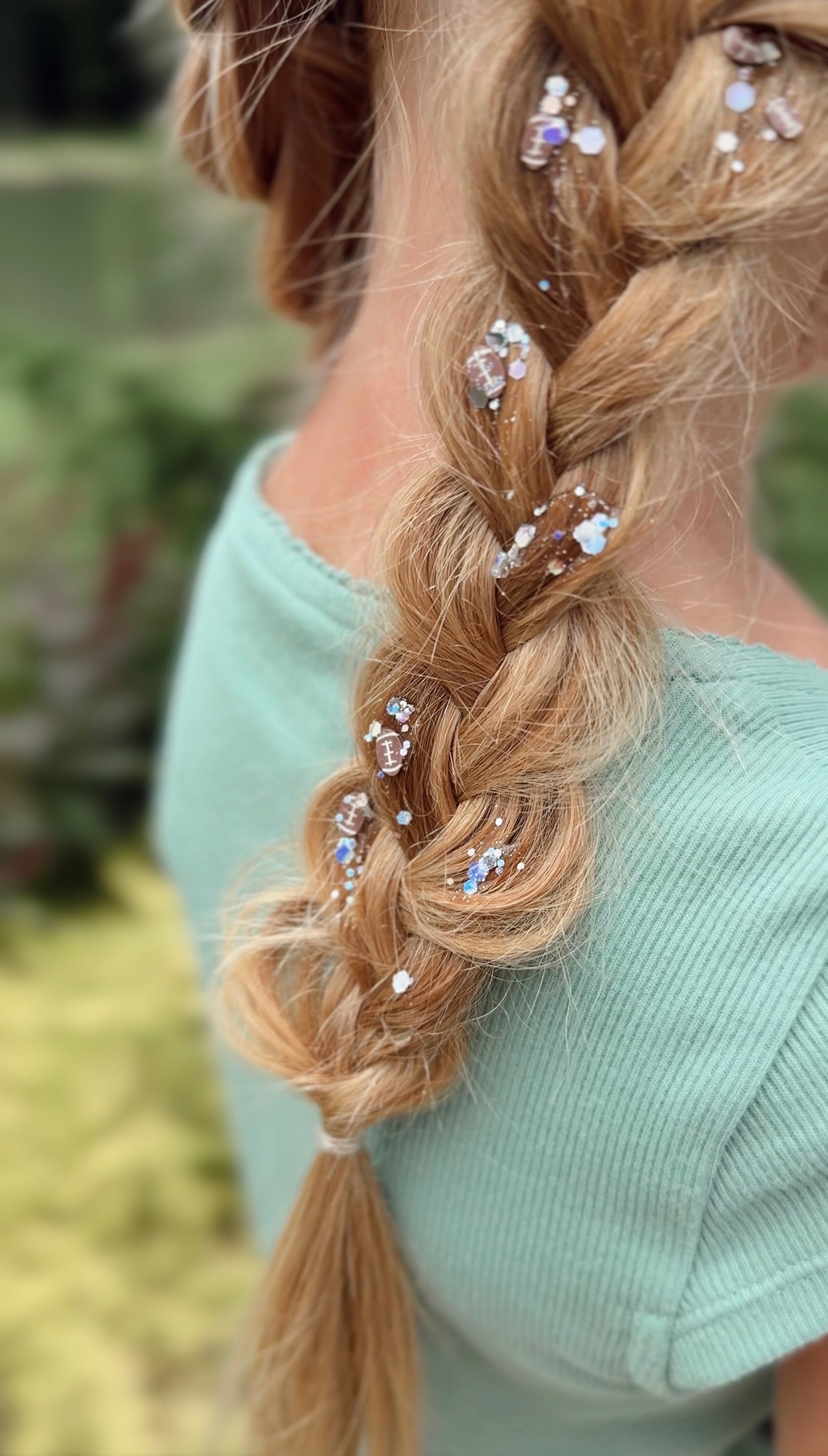 Close-up of blonde braid with Pixie Paste Friday Night Lights hair glitter and tiny football shapes, non-toxic sparkle gel for game day. Football Hair Glitter